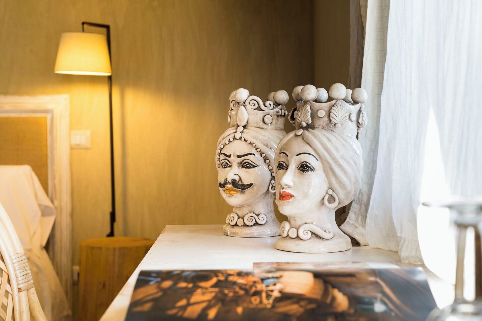 Due sculture di teste in ceramica su un tavolo, con una lampada sullo sfondo.