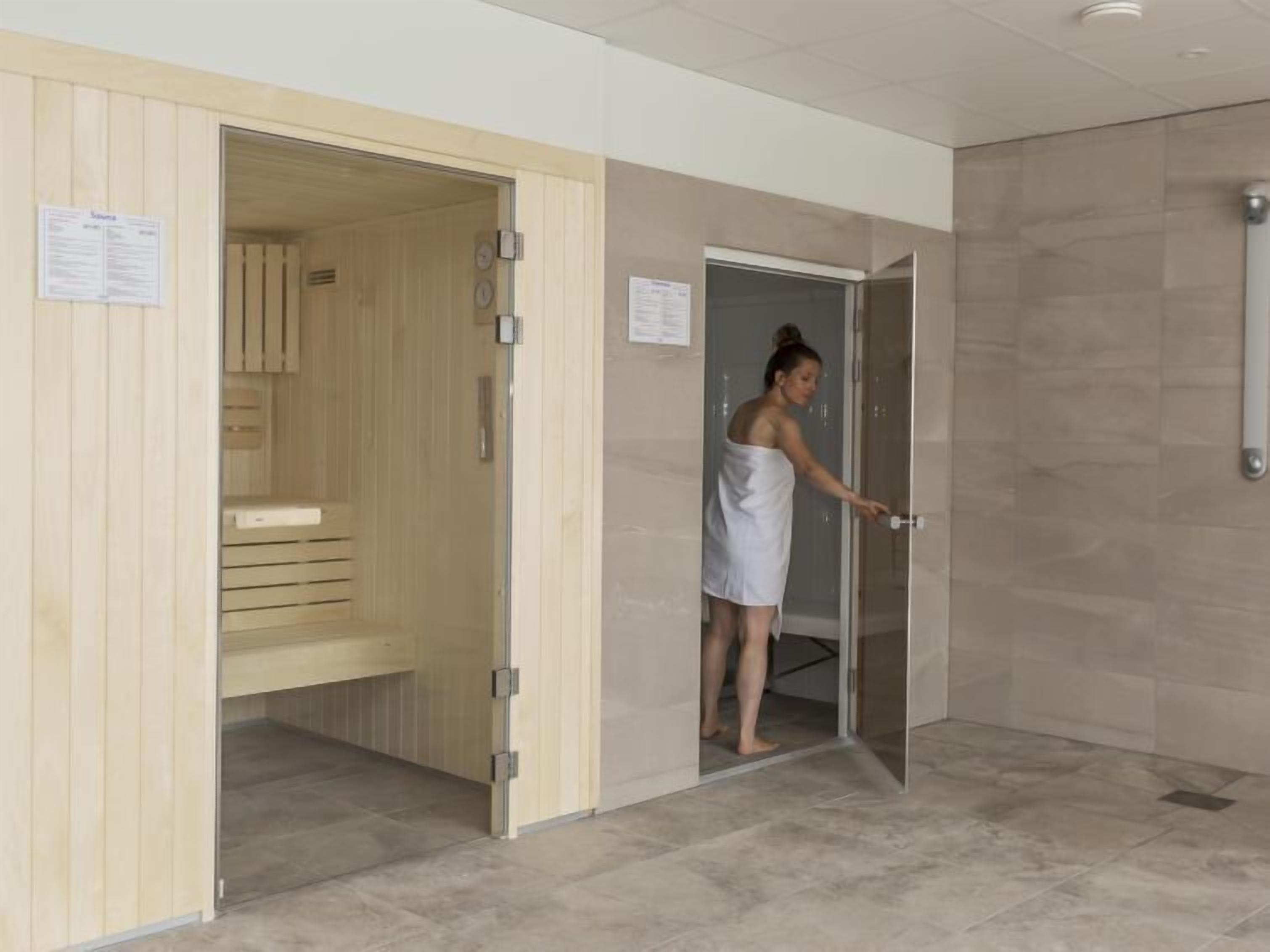 Une salle de spa dotée d’un sauna en bois, d’une porte en verre et d’un sol carrelé.