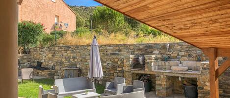 Un patio exterior con muros de piedra, una pérgola de madera y una chimenea de piedra.