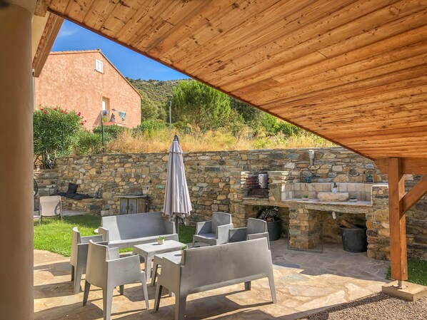 An outdoor patio with stone walls, a wooden pergola, and a stone fireplace.