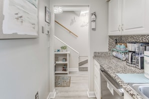 A kitchen with white cabinets, a granite countertop, a coffee maker, and a tiled backsplash.
