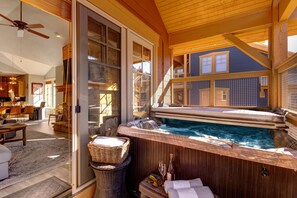 A hot tub with a wooden deck, a wicker basket, and a bottle of wine.