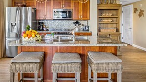 Une cuisine moderne avec des meubles en bois, des appareils en acier inoxydable, un plan de travail en granit et trois tabourets en osier.