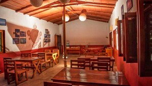 Un restaurant avec des tables et des bancs en bois, un plafond haut avec des poutres apparentes et des luminaires fixés aux murs.