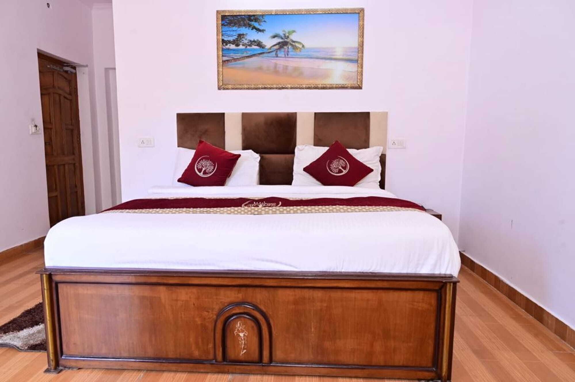 Una cama grande con cabecera de madera, ropa de cama blanca y dos almohadas rojas con un logo de árbol.