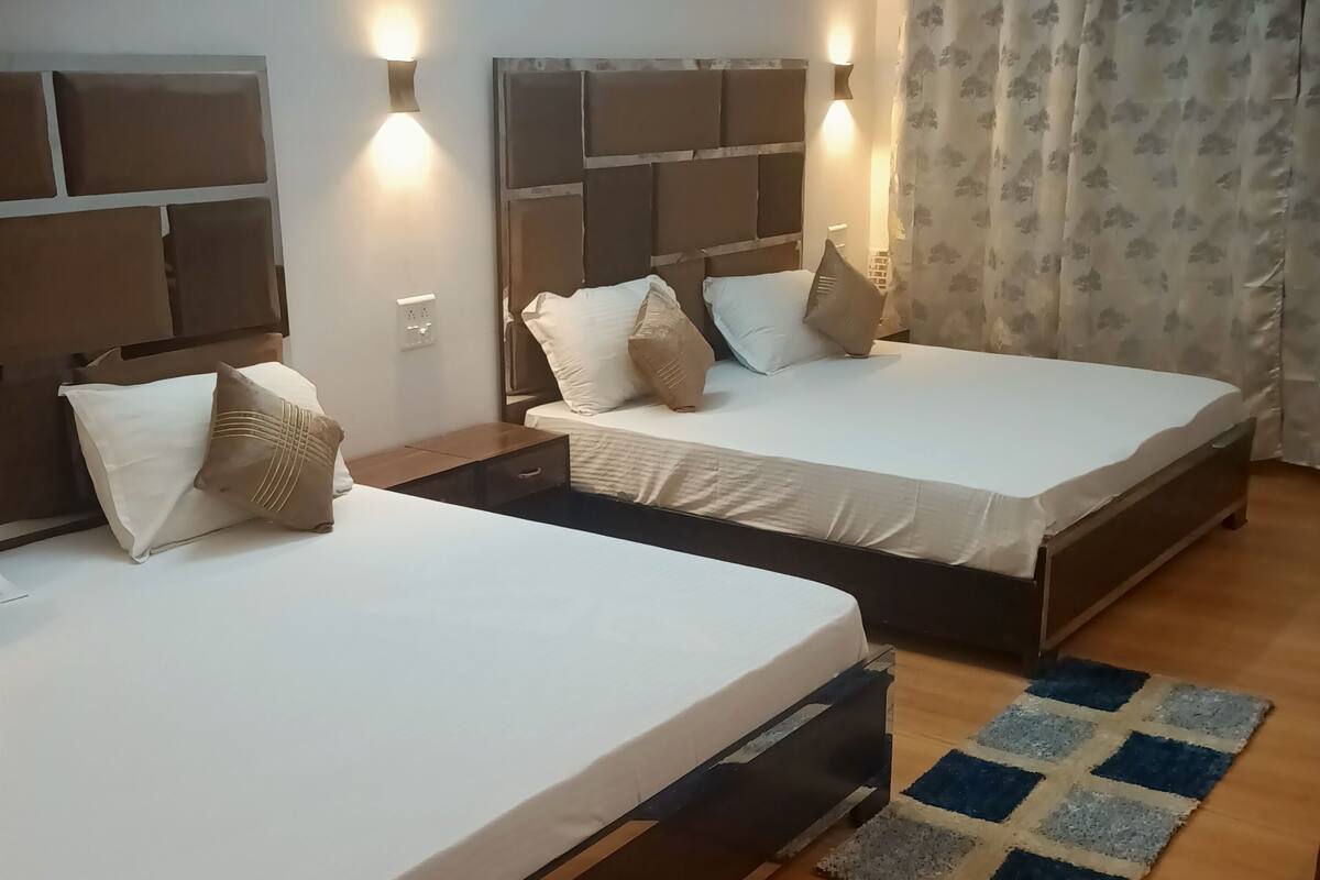 Een hotelkamer met twee bedden, houten vloeren en een kamerbreed gordijn met een patroon.
