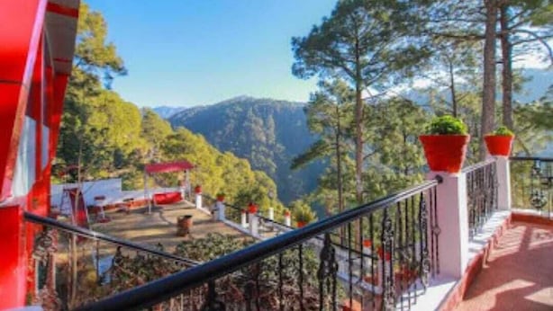 Un balcon donnant sur un paysage montagneux, avec une balustrade rouge et des plantes en pot.