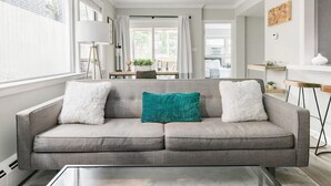 A modern living room with a grey sofa, a glass coffee table, and a view of the outside through large windows. - Inviting Stylish Home with Covered Patio (Chicago)