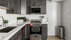 A modern kitchen with dark cabinets, a stainless steel stove, a microwave, and a dishwasher. - Inviting Stylish Home with Covered Patio (Chicago)