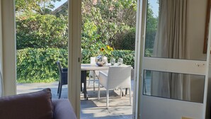 An open sliding glass door leading to an outdoor patio area with a table and chairs, surrounded by greenery. - Very spacious and cosy holiday home (Venlo)