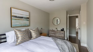 A bedroom with a bed, pillows, a dresser, a mirror, and a painting on the wall.