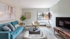 A modern living room with a teal sofa, a round coffee table, and a TV stand.