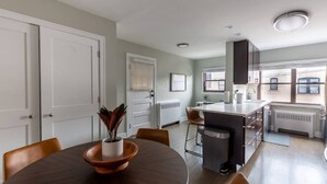 A modern kitchen with a central island, white cabinetry, and a dining area with a round table and chairs.