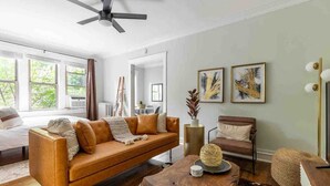 A modern living room with a leather sofa, a wooden coffee table, and a cowhide rug. There are framed artworks on the wall and a ceiling fan. - Rustic Studio Apartment in the Heart of Lincoln Square (Chicago)