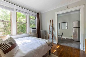 A bedroom with a bed, a radiator, a window with curtains, and a view of the outdoors. - Rustic Studio Apartment in the Heart of Lincoln Square (Chicago)