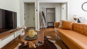 A living room with a television, a brown sofa, a wooden coffee table, and a large mirror on the wall. - Rustic Studio Apartment in the Heart of Lincoln Square (Chicago)