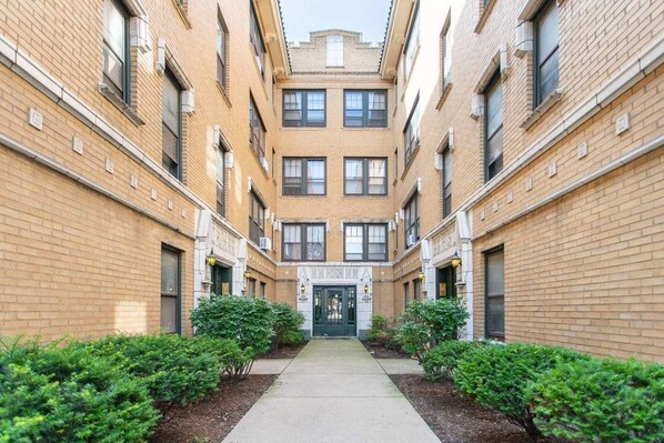 Stylish brick building with a central entrance and multiple windows on each floor, set amidst well-maintained surroundings.