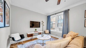 A modern living room with a sofa, a coffee table, a TV, and a window with curtains. - Beautiful and Comfy 1BR in Lincoln Square (Chicago)