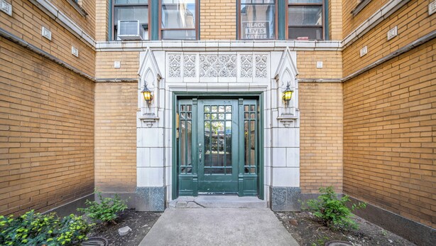 A building entrance with a green door, brick walls, and a small garden area. - Beautiful and Comfy 1BR in Lincoln Square (Chicago)