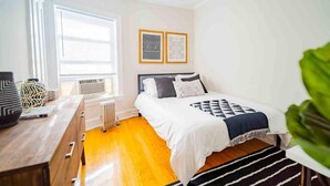 A bedroom with a bed, a desk, a radiator, and two framed pictures on the wall. - Stylish and Comfy Retreat 10 Minutes from Wrigley (Chicago)