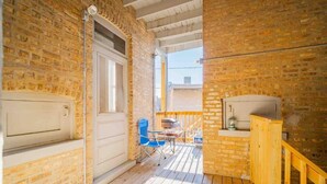 A balcony with a brick wall, a wooden railing, a white door, and a blue chair. - Stylish and Comfy Retreat 10 Minutes from Wrigley (Chicago)