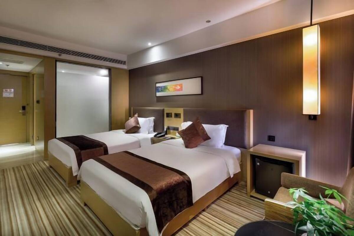 A hotel room with two beds, a small desk, a television, and a wall-mounted artwork.