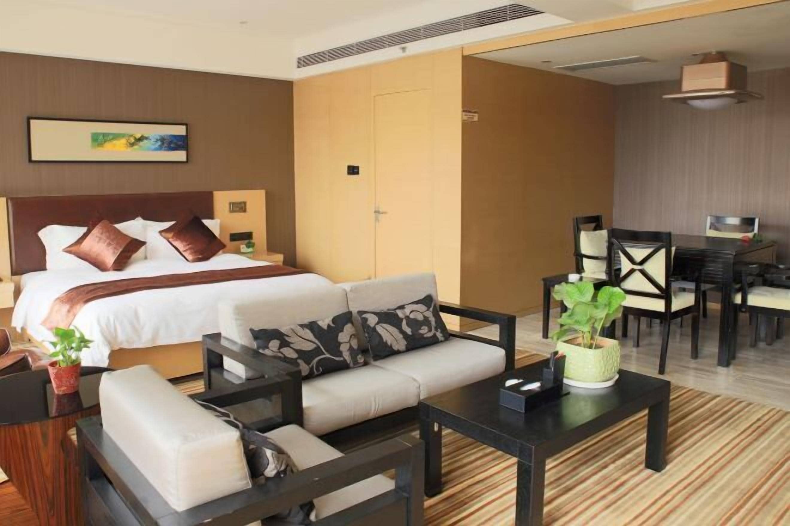 A hotel room with a bed, sofa, dining table, chairs, and a potted plant.
