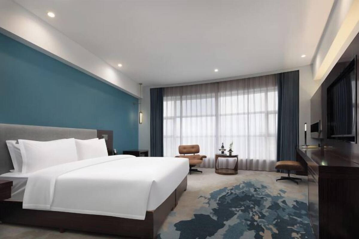 A modern hotel room with a large bed, a desk, a chair, and a TV.