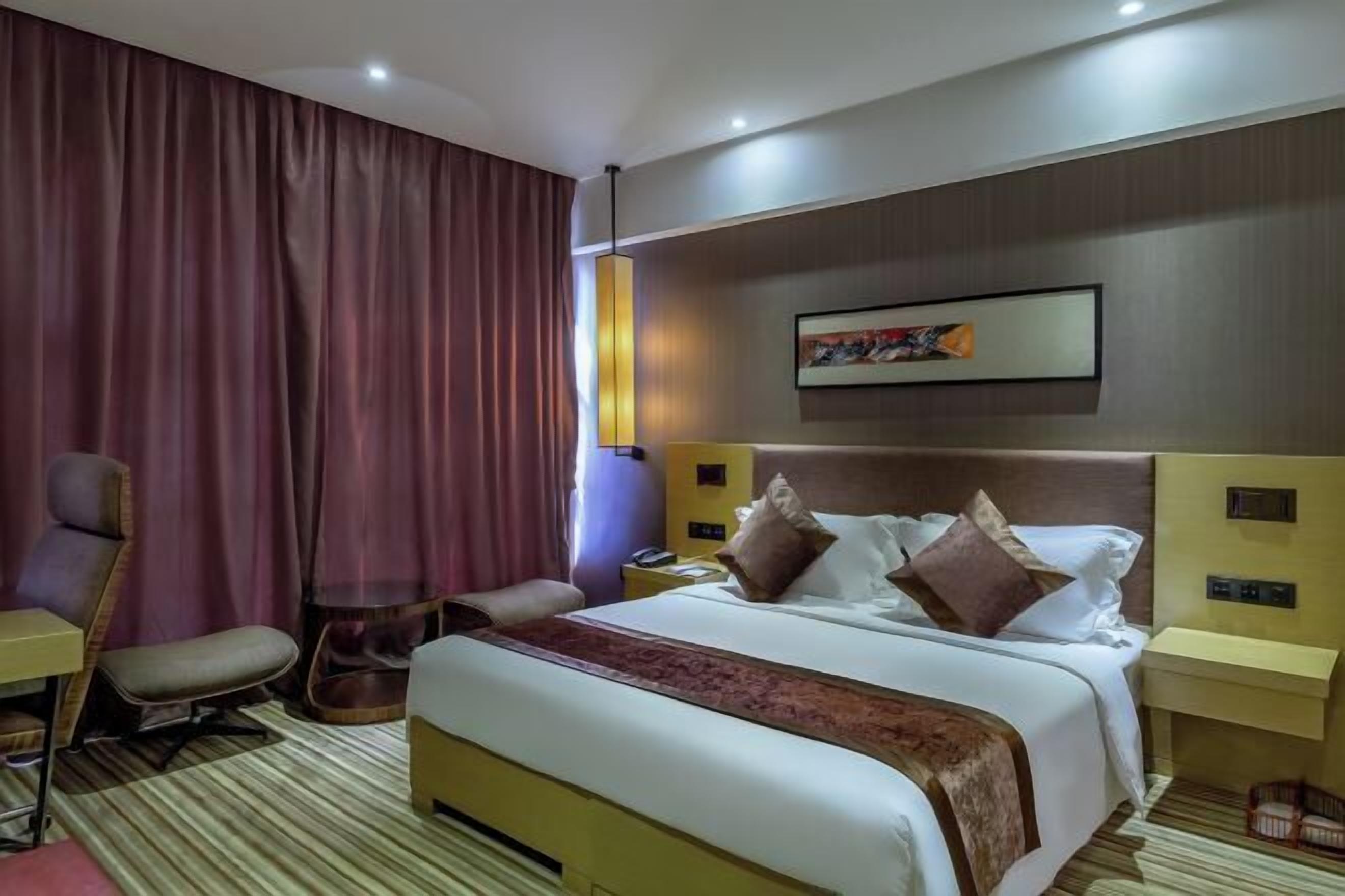 Une chambre d’hôtel comprenant un lit, un bureau, une chaise, une table de chevet et une grande fenêtre avec des rideaux.
