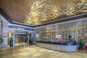 Un moderno vestíbulo de hotel con una recepción, una gran instalación de luces abstractas y un piso de madera pulida.