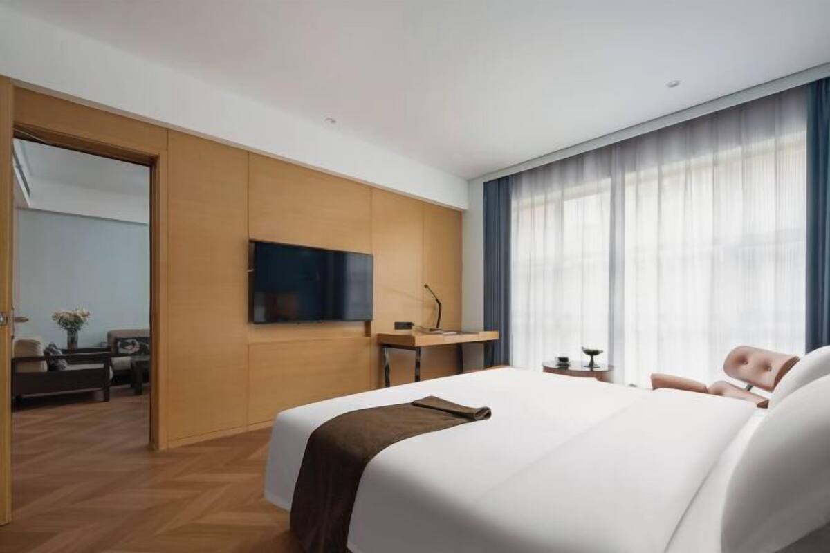 A hotel room with a bed, a desk, a television, and a view of the outdoors.