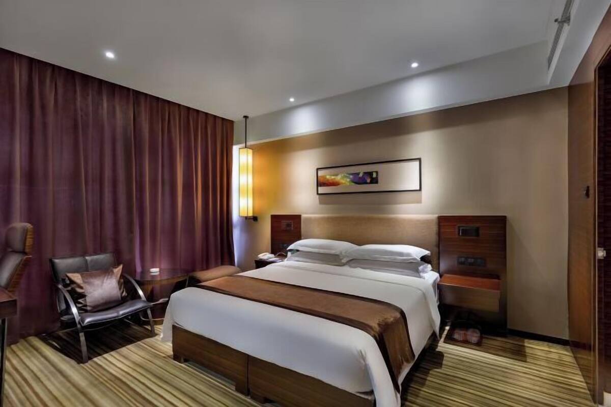 A hotel room with a large bed, a chair, a bedside table, and a wall-mounted artwork.