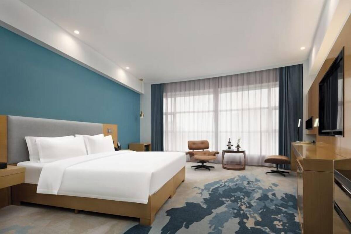 A hotel room with a large bed, a desk, a chair, and a TV.