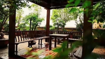 An outdoor wooden deck with benches and tables, surrounded by greenery.