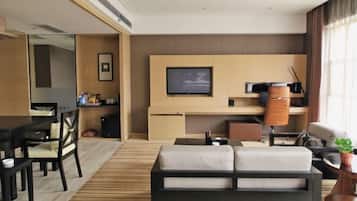 A modern hotel room with a sofa, a dining table, chairs, a TV, and a small plant.