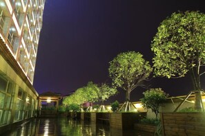 A hotel corridor with a covered walkway, trees, and a building with illuminated windows. - Hengchu Sunshine Hotel (Ningxiang)