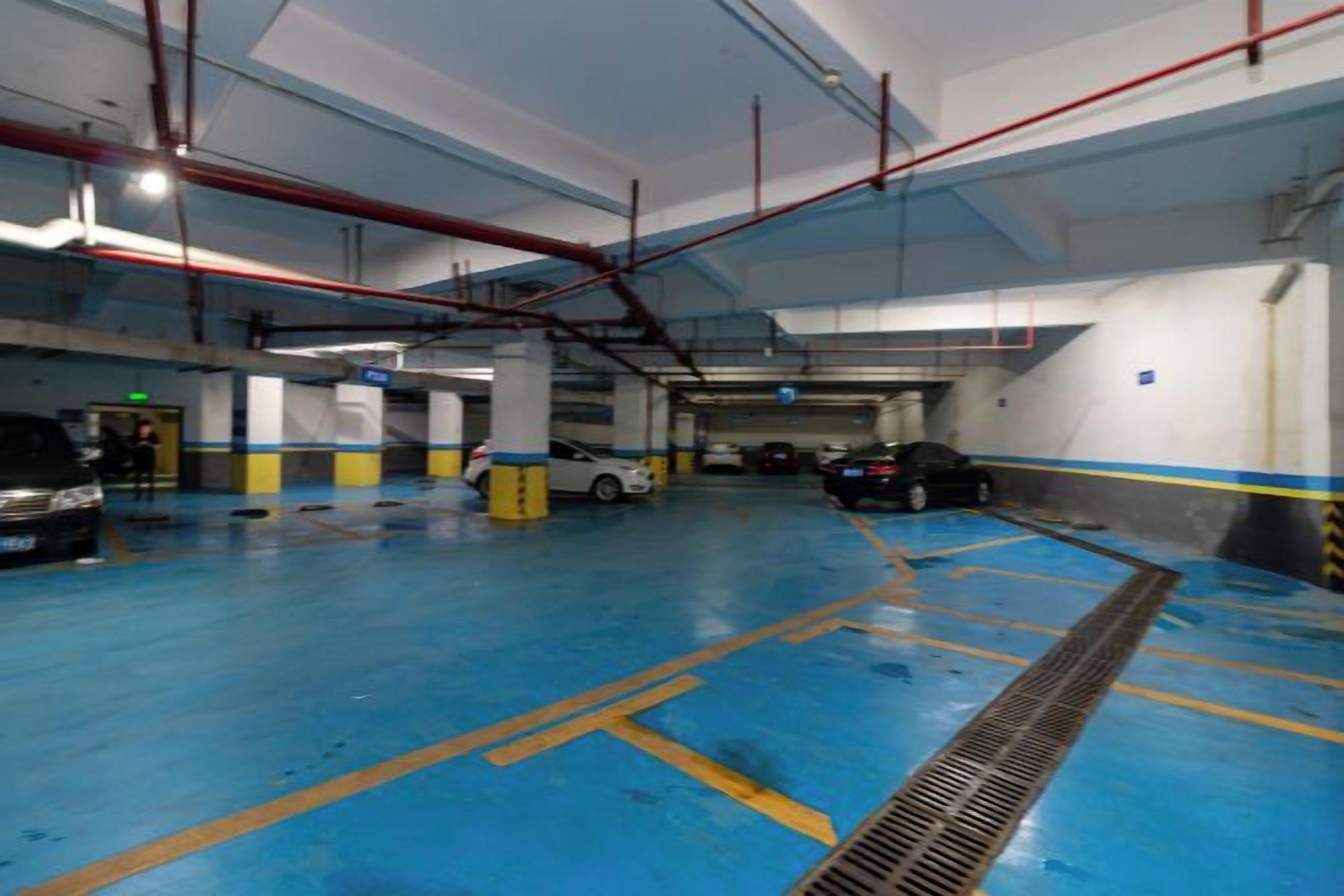Un estacionamiento subterráneo con varios niveles, pilares de hormigón y suelo azul con marcas amarillas.
