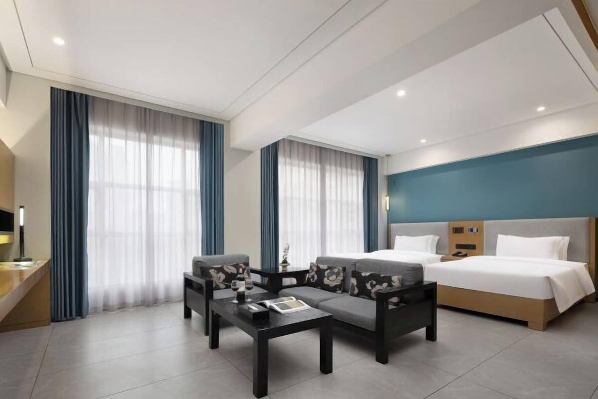 A modern hotel room with a bed, two sofas, a coffee table, and a desk with a lamp.