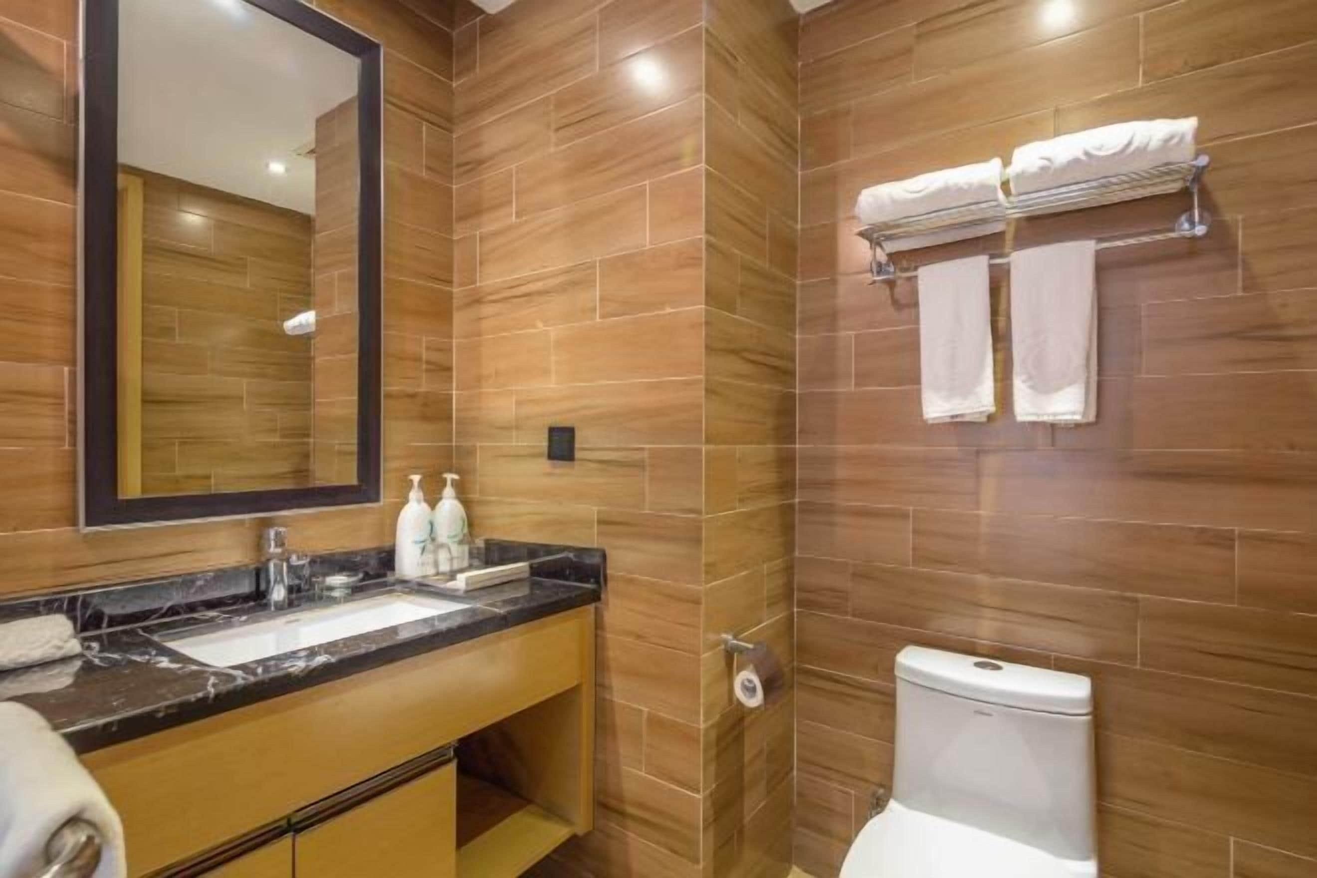 Un baño moderno con lavamanos de mármol, paredes de madera, inodoro y perchero.