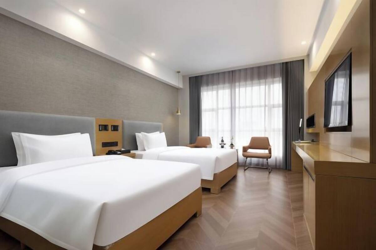 A hotel room with two beds, a desk, a chair, and a TV.