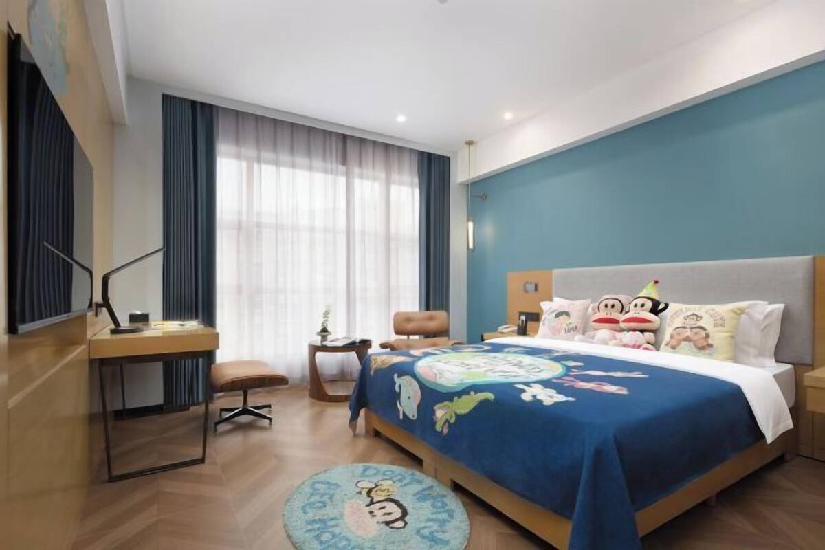 A bedroom with a bed, a desk, a chair, a small table, and a round rug.