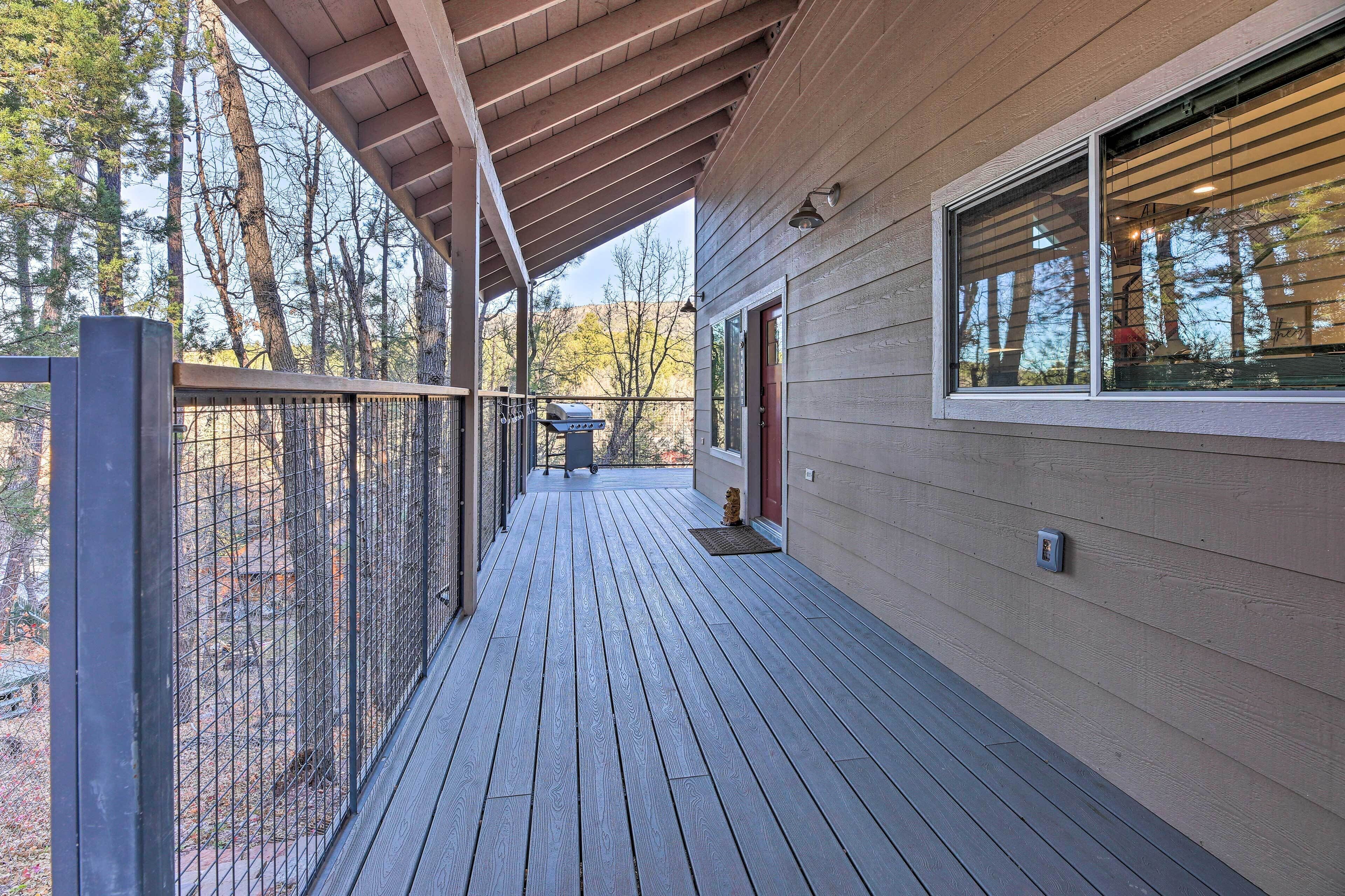 A wooden deck with a metal railing, a barbecue grill, and a door leading to a covered area.