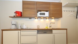 A compact kitchen with wooden cabinets, a microwave, a coffee maker, and a dishwasher. - House Sarah 05, Germany (Sylt)