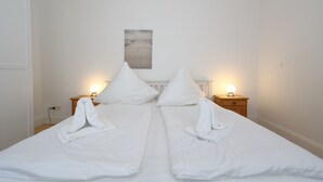 A neatly made double bed with white linens, two bedside tables with lamps, and a framed picture on the wall. - House Sarah 05, Germany (Sylt)