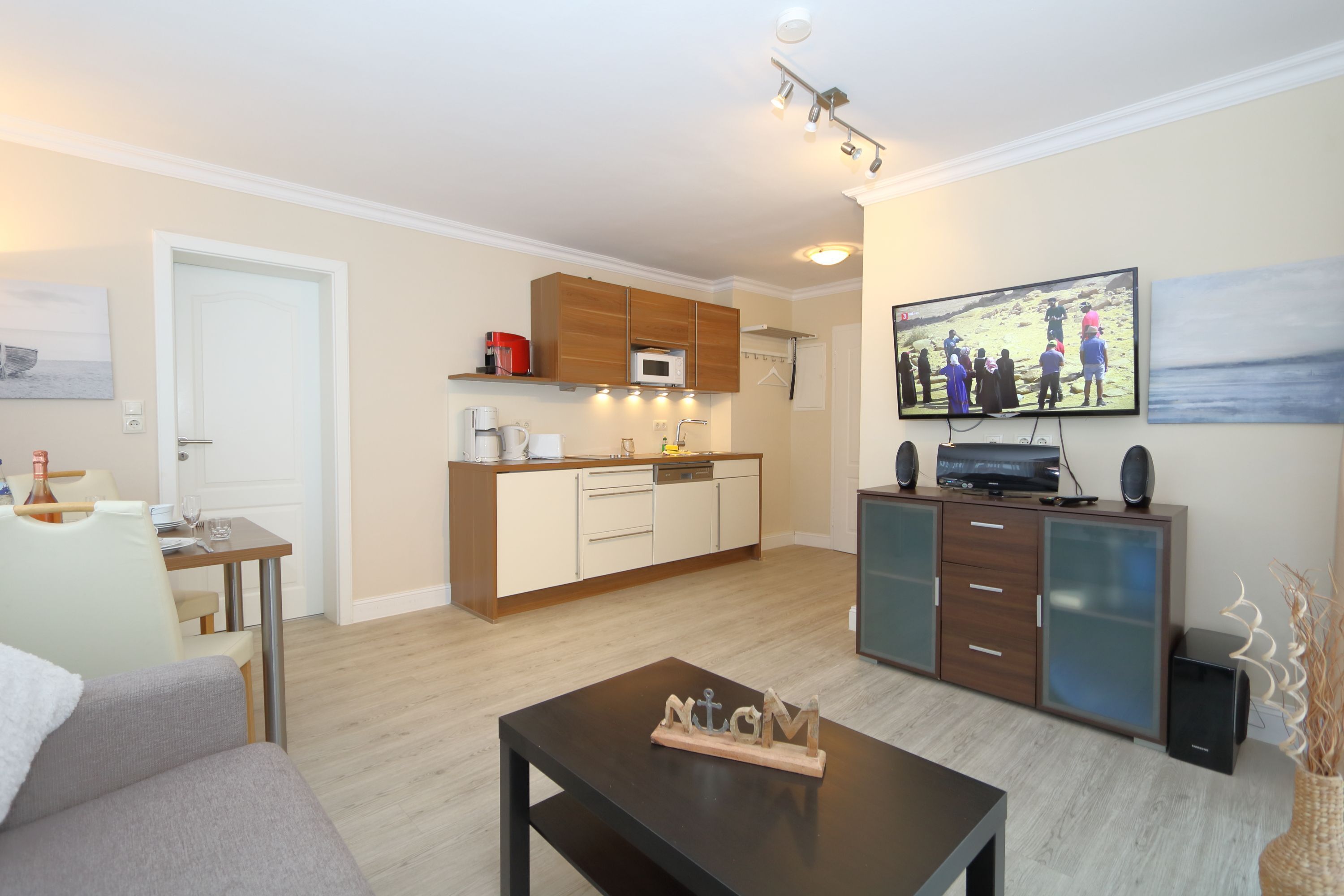 A modern living room with a sofa, a coffee table, a TV, and a kitchen area with cabinets and a microwave.