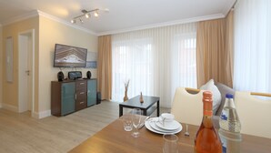 A hotel room with a dining table set for two, a television on a cabinet, and a sofa with a cushion. - House Sarah 05, Germany (Sylt)