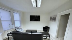 A modern living room with a black leather sofa, a coffee table, and a flat-screen TV mounted on the wall.