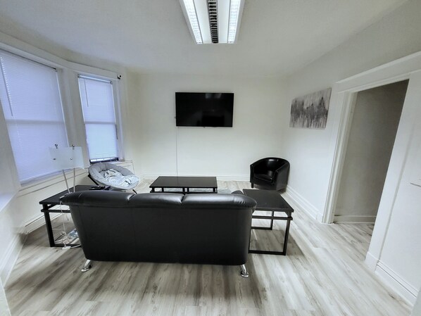 A modern living room with a black leather sofa, a coffee table, and a flat-screen TV mounted on the wall. - 1 private bedroom+ bath
super fast internet, txt2 (Denver)