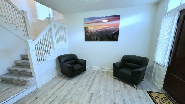 A living room with a staircase, two black armchairs, a wooden floor, and a sunset painting on the wall.