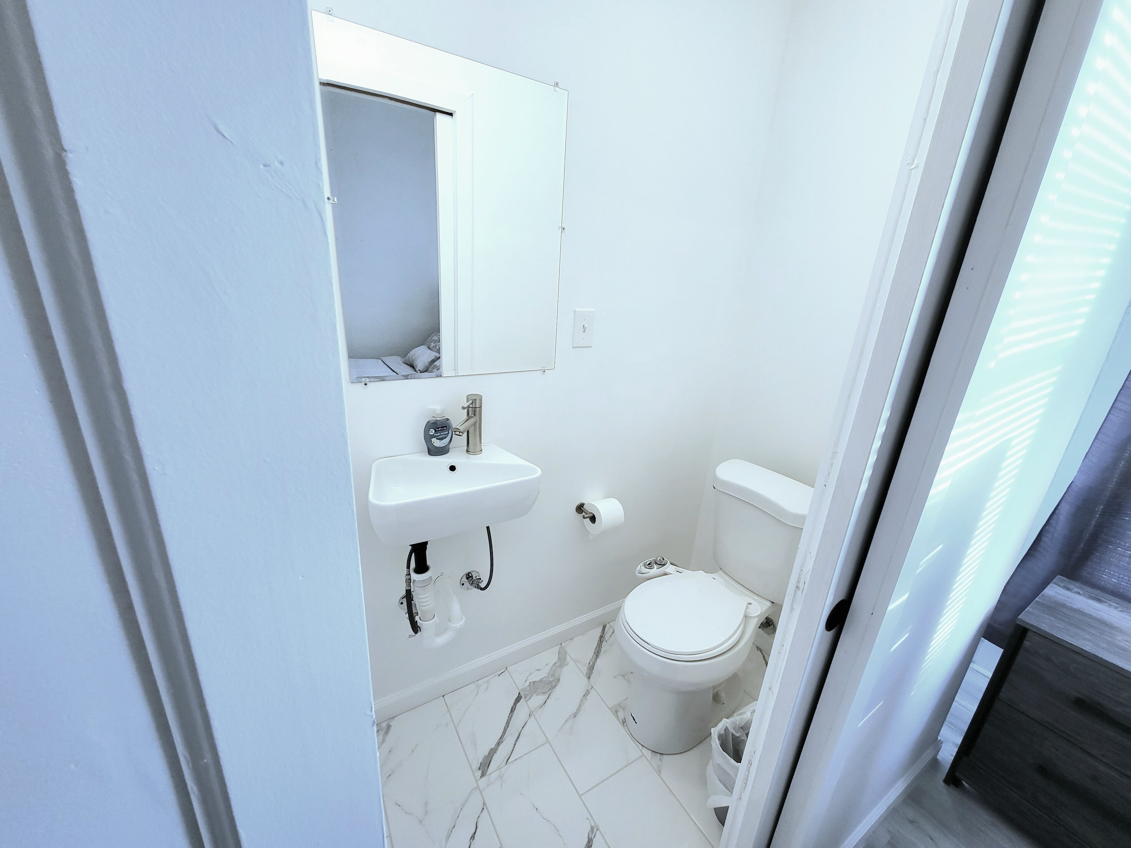 A small, white bathroom with a sink, mirror, and toilet.
